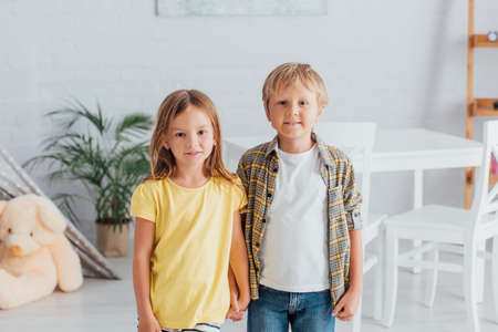 girl in yellow t-shirt with brother in plaid shirt looking at camera while standing at homeの写真素材