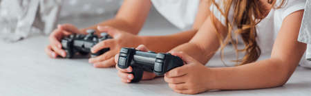 cropped view of brother and sister lying on floor and playing video game with joysticks, horizontal imageの写真素材