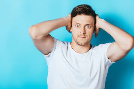 Angry man in white t-shirt covering ears with hands on blue backgroundの写真素材