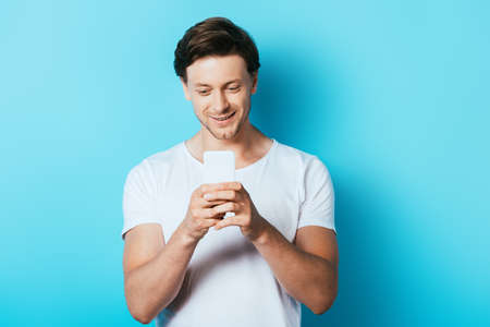 Man in white t-shirt using smartphone on blue background