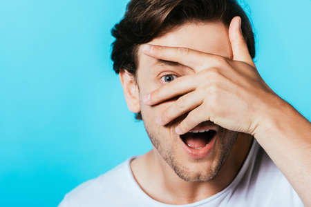 Excited man with hand near face looking at camera isolated on blue