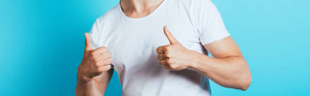 Panoramic shot of man in white t-shirt showing thumbs up on blue backgroundの写真素材