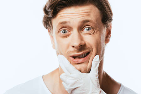 Dermatologist in latex glove touching chin of scared man isolated on white
