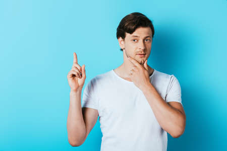 Young man in white t-shirt having idea on blue backgroundの写真素材