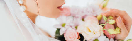 Panoramic shot of bride in pearl earring and veil touching bouquet