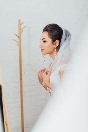 Selective focus of brunette bride in pearl earring wearing veil at homeの写真素材
