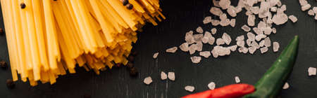 close up view of raw Italian spaghetti with salt on black background, panoramic shot