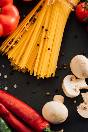 close up view of raw Italian spaghetti with vegetables on black backgroundの写真素材