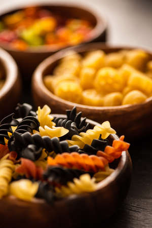 selective focus of colorful raw fusilli pasta in wooden bowlの写真素材