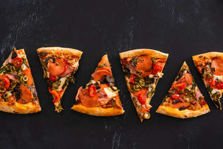 top view of delicious Italian pizza slices with vegetables and salami on black background