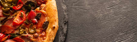 top view of delicious Italian pizza with vegetables and salami on black wooden background, panoramic...