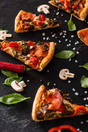 selective focus of delicious Italian pizza slices with salami near vegetables on black backgroundの写真素材