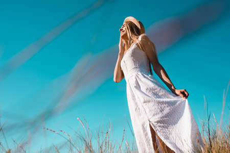 low angle view of sensual woman touching white dress while standing against blue skyの写真素材
