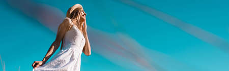 selective focus of young woman touching white dress against blue sky, panoramic concept