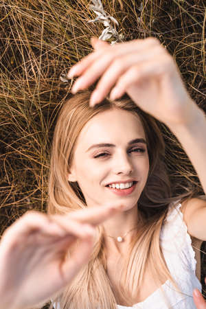 top view of excited blonde woman lying on grass with raised hands and looking at cameraの写真素材