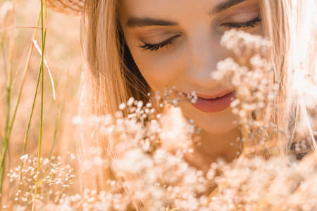 portrait of blonde woman with closed eyes near wildflowers, selective focusの写真素材