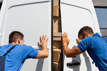 Back view of loaders closing doors of truck with cardboard boxes on urban streetの写真素材