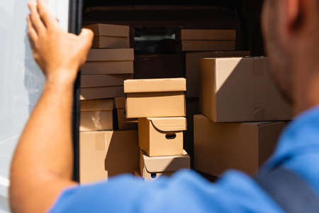 Cropped view of loader standing near cardboard boxes in truck outdoors