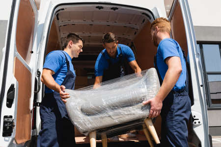 Loaders unloading armchair in stretch wrap from truck on urban street