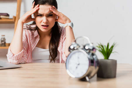 selective focus of stressed woman touching head near alarm clock and plant