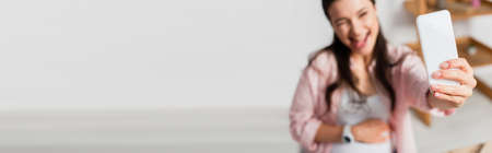 panoramic crop of pregnant woman sticking out tongue while taking selfieの写真素材