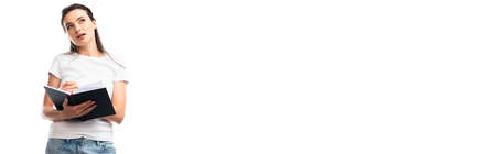 panoramic orientation of thoughtful woman in white t-shirt holding notebook and pen isolated on whiteの写真素材