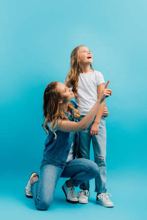 excited girl looking away near mother pointing with finger on blue