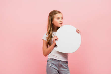 pensive girl in white t-shirt and jeans holding thought bubble and looking away isolated on pinkの写真素材