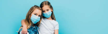 panoramic concept of child in white t-shirt and mother in medical masks looking at camera isolated on blueの写真素材