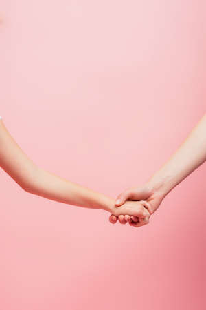 partial view of woman and kid holding hands isolated on pink with copy spaceの写真素材