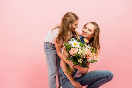child gifting bouquet of flowers to mom and embracing her isolated on pinkの写真素材