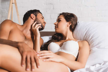 Selective focus of seductive woman touching chin of shirtless man on bedの写真素材