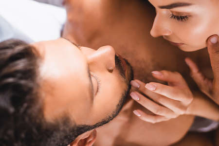 Selective focus of shirtless man touching face of young woman on bed