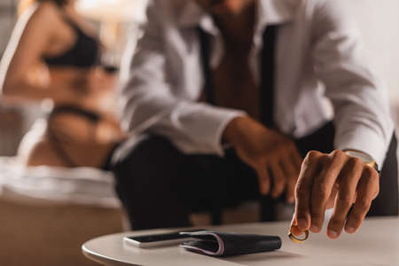 Selective focus of man putting wedding ring near wallet and smartphone on coffee table near woman in...