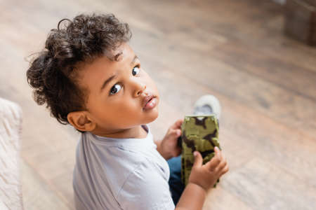 overhead view of curly african american child looking at camera while holding toy