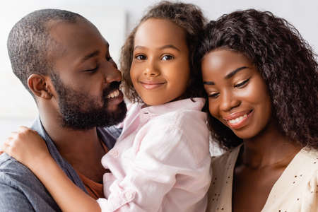 african american man holding daughter on hands near mother at home