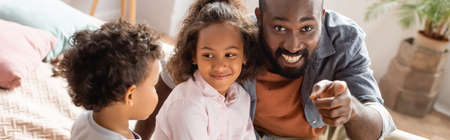 horizontal image of african american man pointing with finger near kids at home