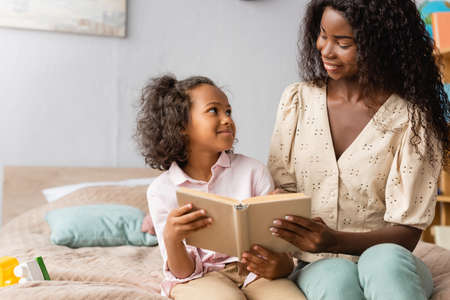 african american mom and child looking at each other while reading book togetherの写真素材