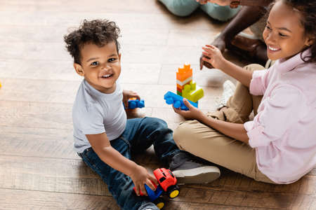 high angle view of african american brother and sister playing with toy truck and building blocks on floor at homeの写真素材