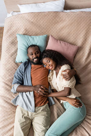 top view of african american husband and wife in casual clothes resting in bed and looking at cameraの写真素材