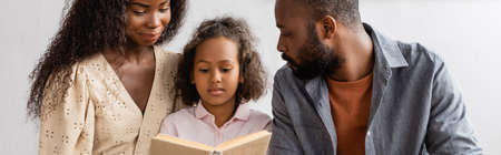 panoramic shot of african american parents near focused daughter reading bookの写真素材