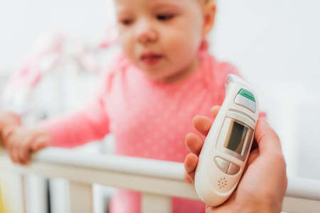 Selective focus of woman holding inhaler near daughter in crib