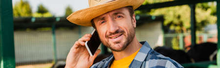 horizontal concept of rancher in straw hat looking at camera while talking on smartphone