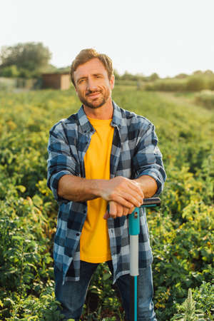 farmer in plaid shirt looking at camera while standing with shovel in field