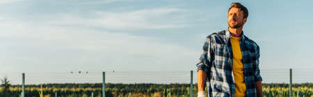 website header of rancher in plaid shirt looking away while standing in field on farm