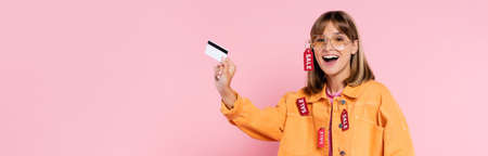 Horizontal crop of excited young woman in sunglasses and jacket with price tags holding credit card...