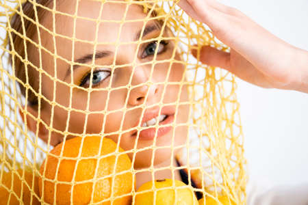 portrait of woman in string bag with citrus fruitsの写真素材