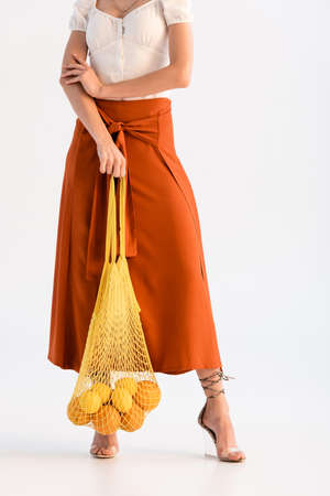 cropped view of fashionable woman posing with citrus fruits in string bag isolated on white