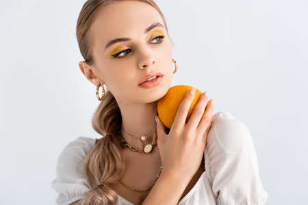 elegant blonde woman posing with orange and looking away isolated on whiteの写真素材