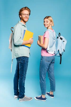 students with backpacks holding notebooks and books while standing on blueの写真素材